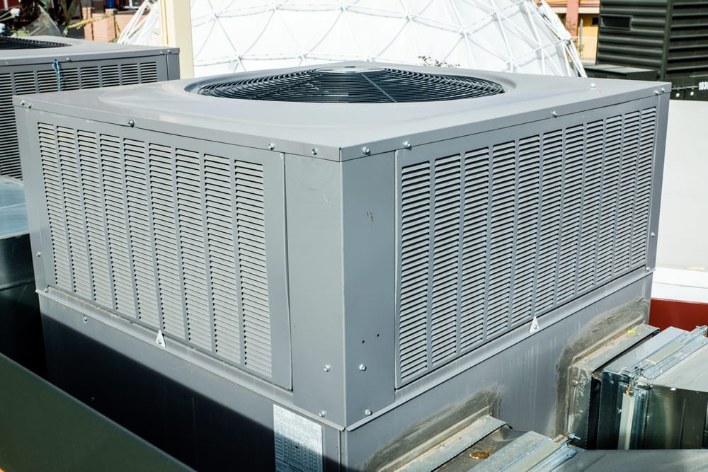A large metal air conditioning unit on a rooftop, surrounded by additional HVAC equipment.