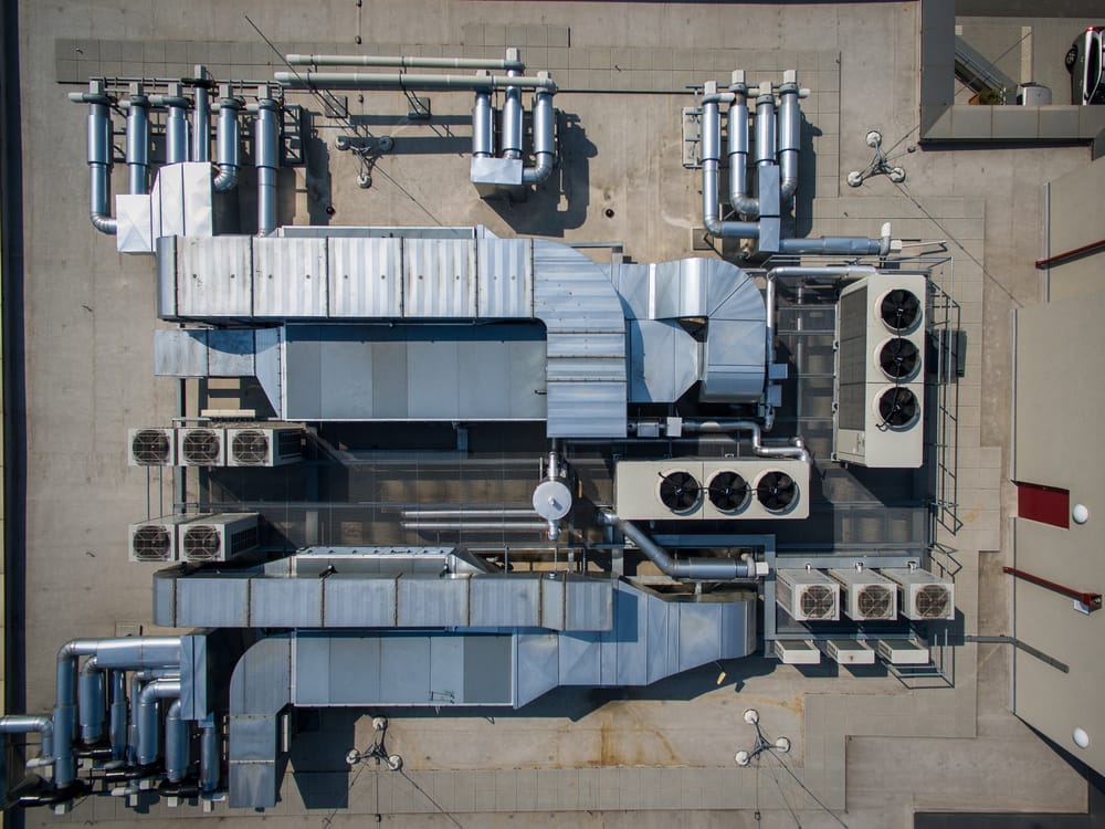 Aerial view of a complex rooftop HVAC system with multiple ducts, vents, and fans on a flat industrial roof.