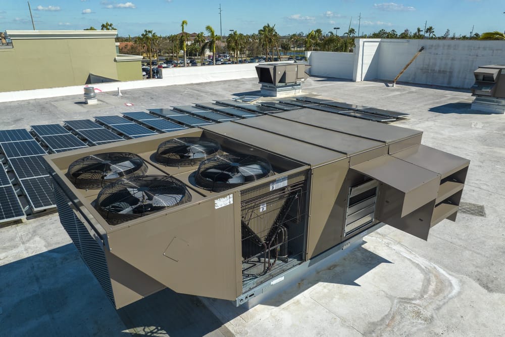 Rooftop view of an industrial HVAC unit surrounded by solar panels under a clear blue sky.