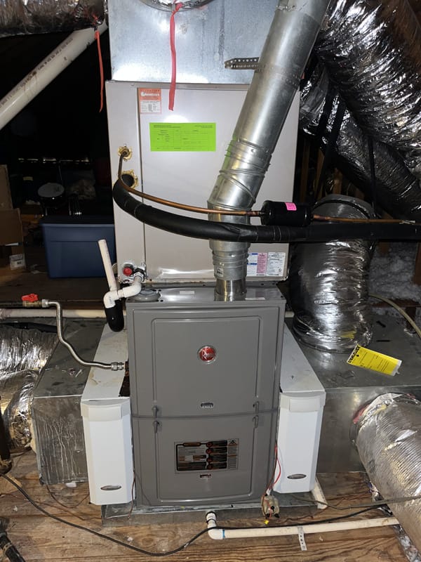 A home HVAC system installed in an attic. The image shows ducts, a furnace, and a water heater, with pipes and insulation visible.