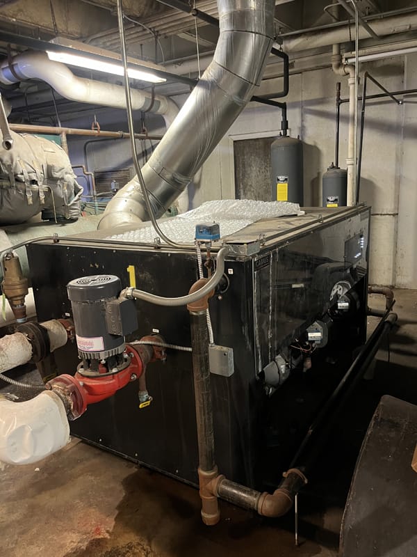 Industrial HVAC unit with pipes and ducts in a mechanical room.