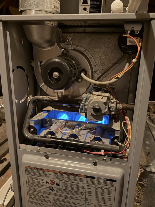 Furnace with panels open, showing blue flames, wiring, and internal components. Warning labels are visible on the lower panel.